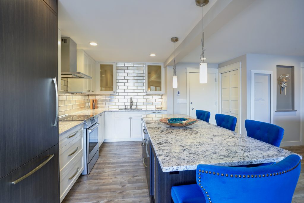 Well appointed kitchen features a large kitchen island topped with a gray quartzite countertop and flanked by blue tufted dining chairs with silver nailhead trim.