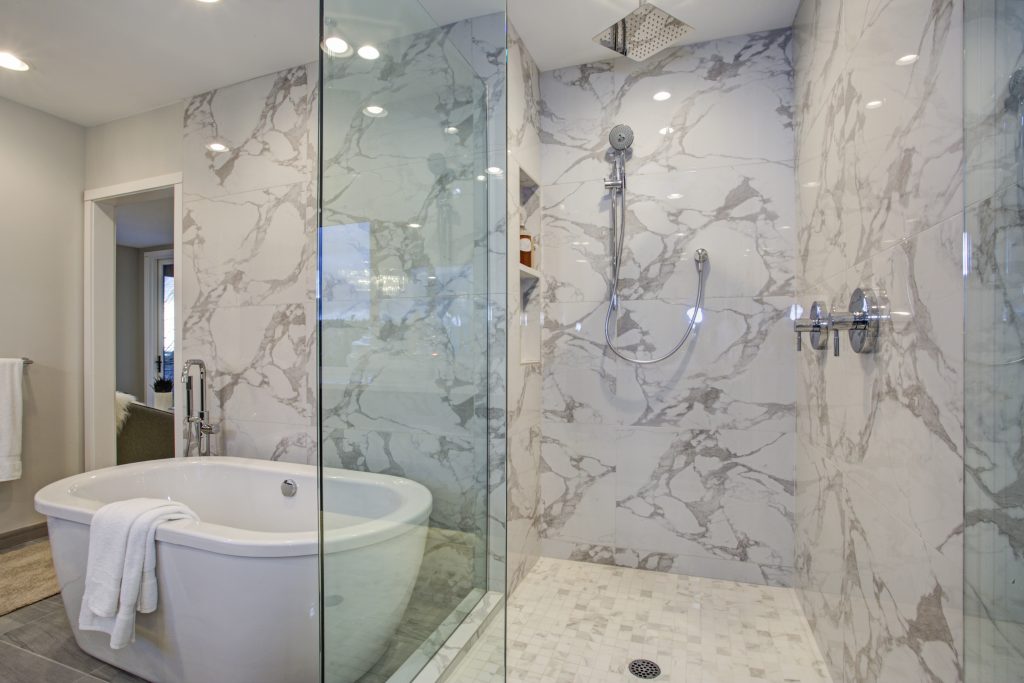 White and gray calcutta marble bathroom design with custom soaking tub and glass walk in shower.